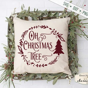 May include: A white cushion with a red design that says "Oh Christmas Tree" in a wreath of greenery. The cushion is sitting on a wooden crate with greenery around it.