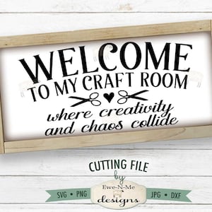 May include: A framed sign with the text "WELCOME TO MY CRAFT ROOM where creativity and chaos collide". The sign is on a white wooden background. The text is in black and the sign is surrounded by a wooden frame.