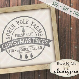 Op de afbeelding: Een wit bord met een grijze cirkel waarop staat "North Pole Farms Fresh Cut Christmas Trees Fir Spruce Cedar". Het bord staat op een houten achtergrond.