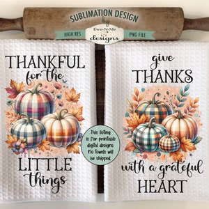 May include: Two white kitchen towels with Thanksgiving-themed designs. The left towel features a plaid pumpkin and the text "Thankful for the little things". The right towel features a plaid pumpkin and the text "Give Thanks with a grateful heart".