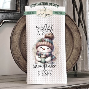 May include: A white kitchen towel with a winter-themed design featuring a snowman holding a cup of hot chocolate. The text "winter wishes snowflake kisses" is printed on the towel.