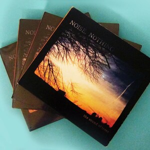 Op de afbeelding: Een stapel van vier cd's met een zonsondergang en takken van bomen op de hoes. De tekst op de hoes luidt "Noise Nothing the sound of trees".
