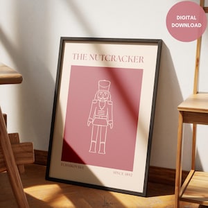 May include: A framed art print featuring a minimalist illustration of a nutcracker soldier in white on a dusty rose background. The text "THE NUTCRACKER" is at the top, with "TCHAIKOVSKY" and "SINCE 1892" at the bottom. A digital download.