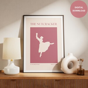 May include: A framed art print featuring a ballet dancer silhouette on a pink background. The text "THE NUTCRACKER" is at the top, with "TCHAIKOVSKY" and "SINCE 1892" at the bottom. The print is displayed on a wooden surface.