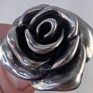 May include: A close-up of a silver-coloured rose sculpture. The metal rose has multiple layers of petals, with a textured surface and a dark, shadowed centre. The rose is a decorative item.