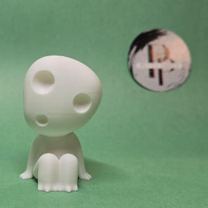 May include: White 3D printed figurine of a character with a large head and three holes. The character is sitting with its legs crossed.