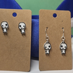 May include: Two pairs of earrings featuring a white cartoon character with black eyes and a mouth. One pair is stud earrings and the other pair is dangle earrings with silver hooks.