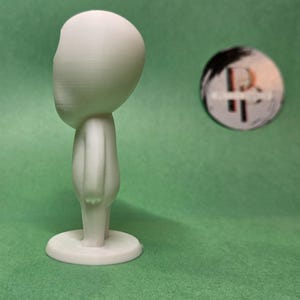 May include: A white 3D printed figurine of a person with a large head and no facial features. The figurine is standing on a round base.