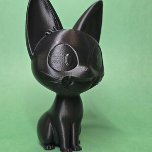 May include: A black 3D printed figurine of a cartoon cat with large eyes and a wide smile. The cat is sitting with its legs tucked under its body.