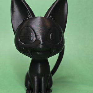 May include: A black 3D printed figurine of a cat sitting with its tail curled around its legs. The cat has large, round eyes and a friendly expression.