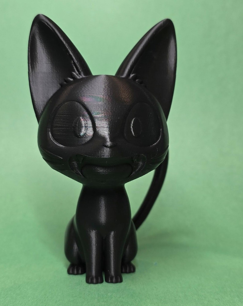 May include: A black 3D printed figurine of a cat sitting with its tail curled around its legs. The cat has large, round eyes and a friendly expression.