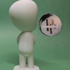 May include: A white 3D printed figurine of a person with a large head and small body. The figurine is standing on a circular base.