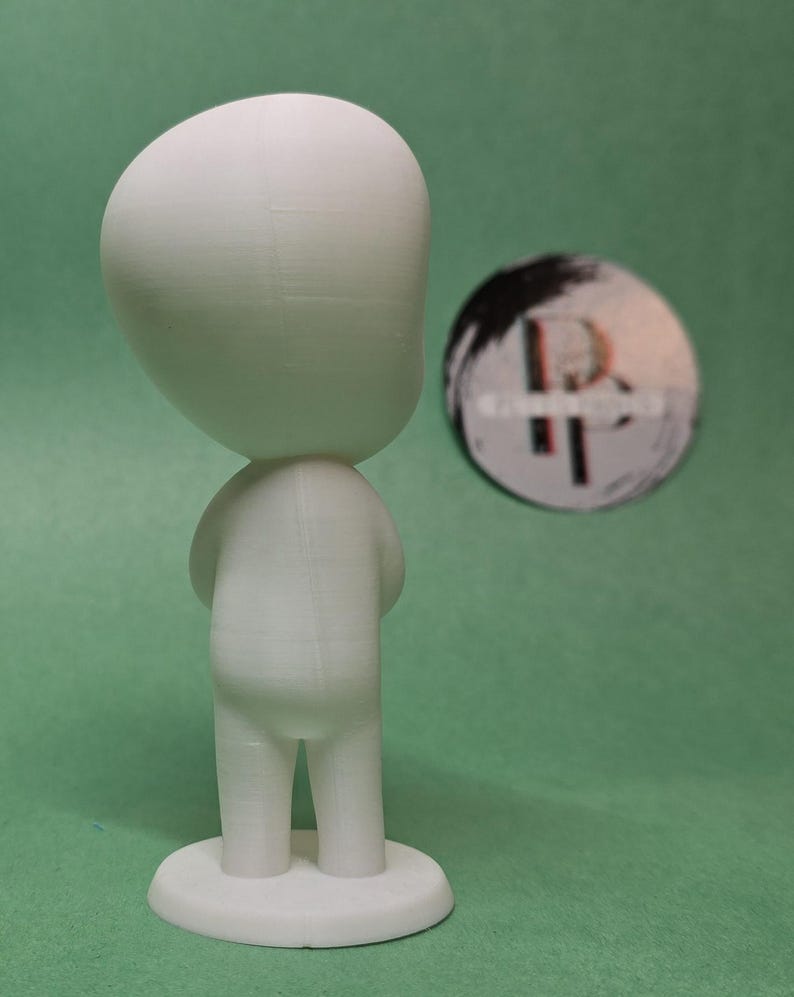 May include: A white 3D printed figurine of a person with a large head and small body. The figurine is standing on a circular base.