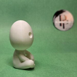 May include: A white 3D printed figurine of a person sitting in a meditative pose with a hole in the head.