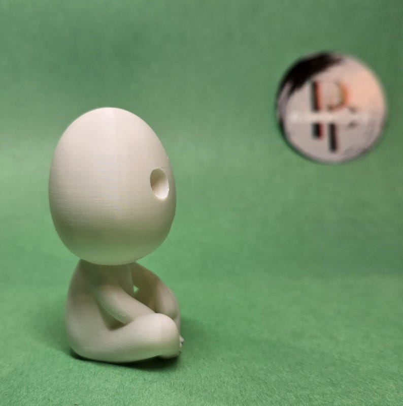 May include: A white 3D printed figurine of a person sitting in a meditative pose with a hole in the head.