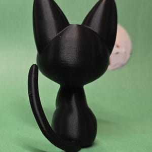 May include: A black cat figurine with a curled tail, sitting on a green surface.