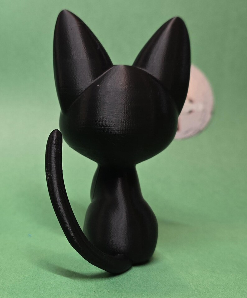 May include: A black cat figurine with a curled tail, sitting on a green surface.