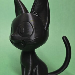 May include: A black 3D printed figurine of a cat sitting with its tail curled around its body. The cat has large eyes and a cute expression.