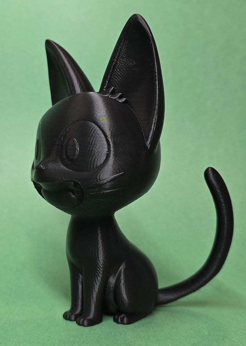 May include: A black 3D printed figurine of a cat sitting with its tail curled around its body. The cat has large eyes and a cute expression.