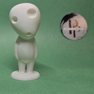 May include: White 3D printed figurine of a character with a large head and two eyes. The figurine is standing on a small base.