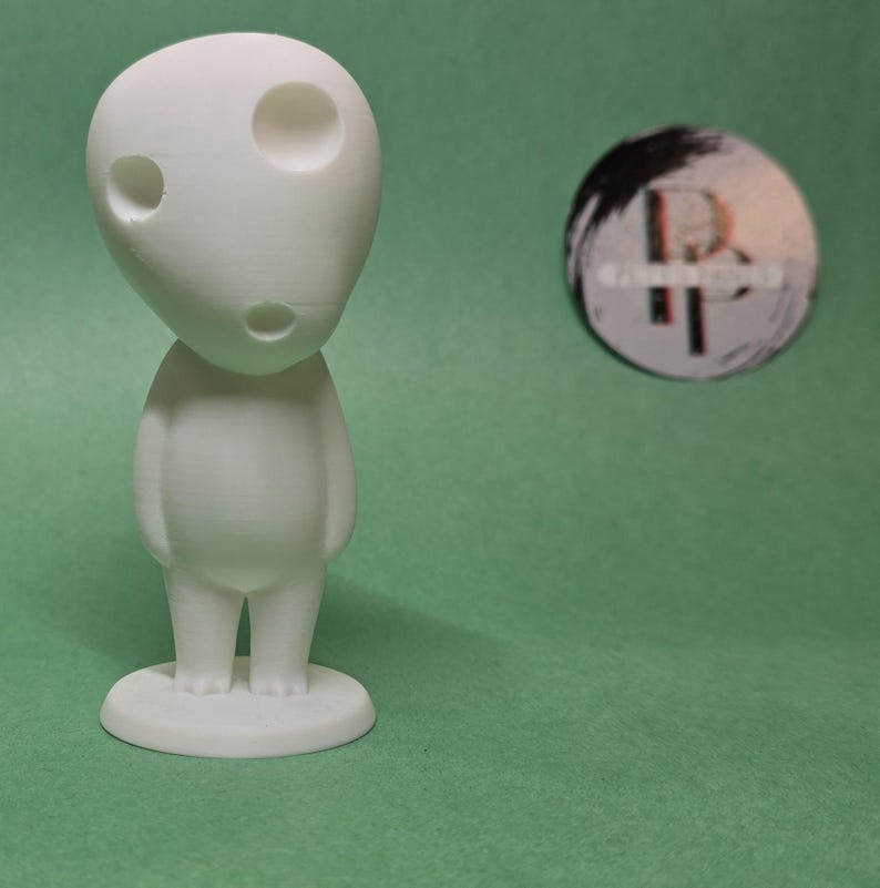 May include: White 3D printed figurine of a character with a large head and two eyes. The figurine is standing on a small base.