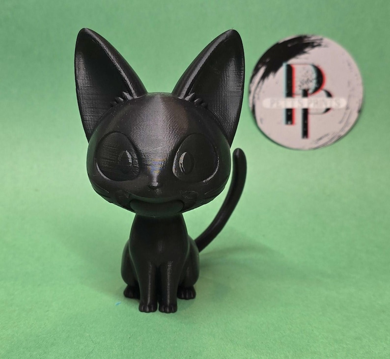 May include: A black cat figurine with large eyes and a small smile. The figurine is made of a smooth, matte black plastic.