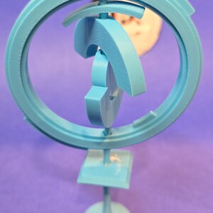 May include: A light blue, 3D printed, abstract sculpture with a circular base and a series of interlocking rings. The sculpture is designed to rotate and spin.