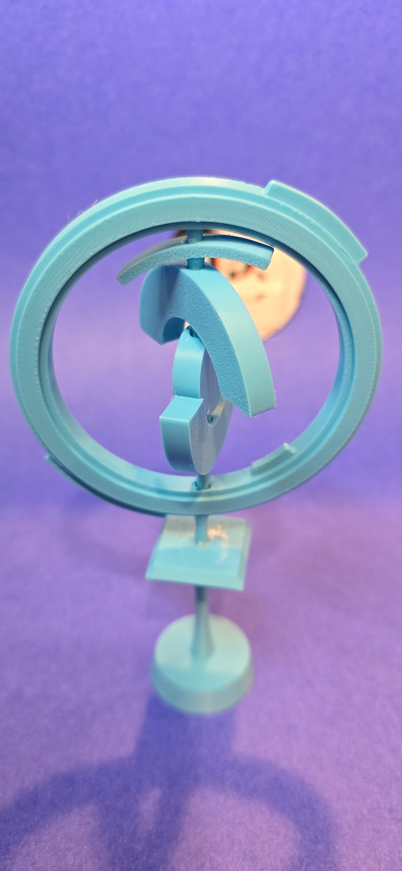 May include: A light blue, 3D printed, abstract sculpture with a circular base and a series of interlocking rings. The sculpture is designed to rotate and spin.
