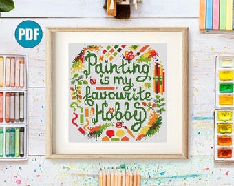 Peut inclure: Une œuvre d'art au point de croix encadrée avec le texte "Painting is my favourite Hobby" entourée de pinceaux, de crayons et de feuilles colorés. L'œuvre est dans un cadre en bois, avec du matériel d'art visible en arrière-plan.