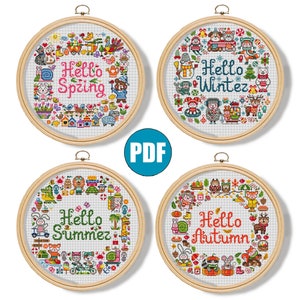 Puede incluir: Cuatro aros de bordado de punto de cruz con marcos de madera. Cada aro presenta un tema estacional: Primavera, Invierno, Verano y Otoño. El texto "Hola" va seguido del nombre de la estación en cada diseño. Los diseños incluyen varios animales y elementos estacionales.