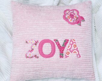 May include: Pink pillow with the name "ZOYA" spelled out in colorful fabric letters. The pillow has a pink flower applique in the top right corner.