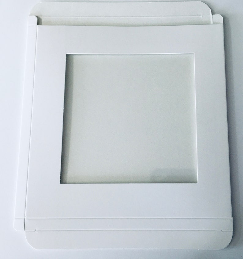 May include: White cardboard box with a square window cut out. The box is designed to hold a square item, such as a photo or a piece of art.