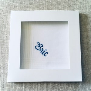 May include: A white handkerchief with a blue embroidered name "Eric" in a white frame.