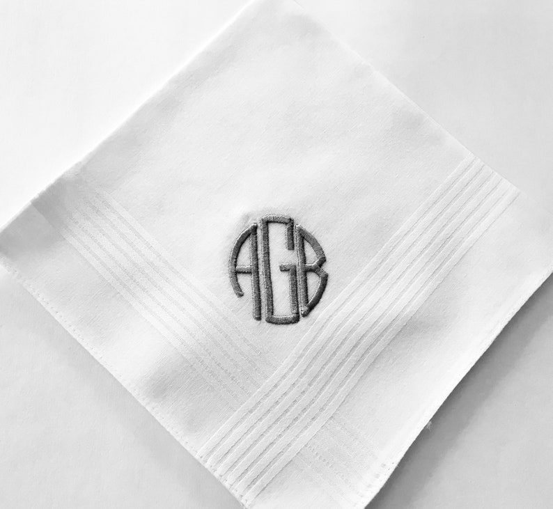May include: White cotton handkerchief with a gray embroidered monogram of the letters "AGB" in a circle.