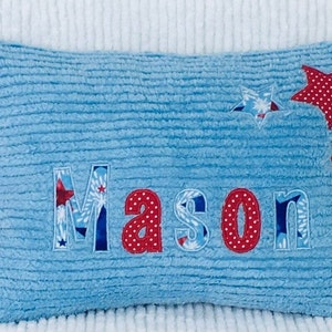 May include: A blue plush pillow with the name "Mason" embroidered in red and white fabric. The pillow is decorated with red and white stars.