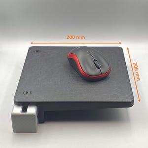 May include: A black computer mouse with red accents rests on a square, dark gray platform. The platform, measuring 7.9 inches by 7.9 inches, is supported by a silver and gray bracket, designed for desk mounting.