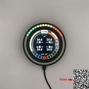 Puede incluir: Un medidor digital redondo con un bisel negro muestra varios puntos de datos, incluyendo números y porcentajes. El medidor tiene una serie de luces de colores y un código QR con la palabra "Video".