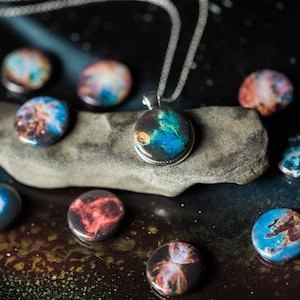 May include: A silver chain necklace with a round pendant featuring a colorful nebula image. The pendant is surrounded by smaller round pendants with similar nebula images.