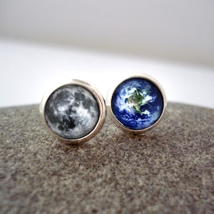 May include: A pair of silver stud earrings with a round image of the moon on one earring and a round image of the earth on the other earring.