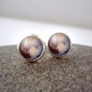 May include: A pair of silver stud earrings with a round, brown, white, and blue image of a planet.