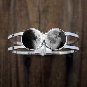 May include: A silver double-band bracelet with two round glass cabochons featuring a black and white image of the moon.