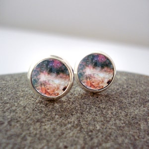 May include: A pair of silver stud earrings with a galaxy-themed design. The earrings feature a round, silver setting with a colorful image of a nebula.