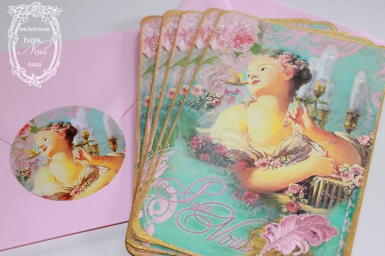 May include: Set of six gold-trimmed cards with a vintage illustration of a woman in a pink and green floral setting. The cards have a glittery finish and the text "Je t'aime" is written in a cursive font.