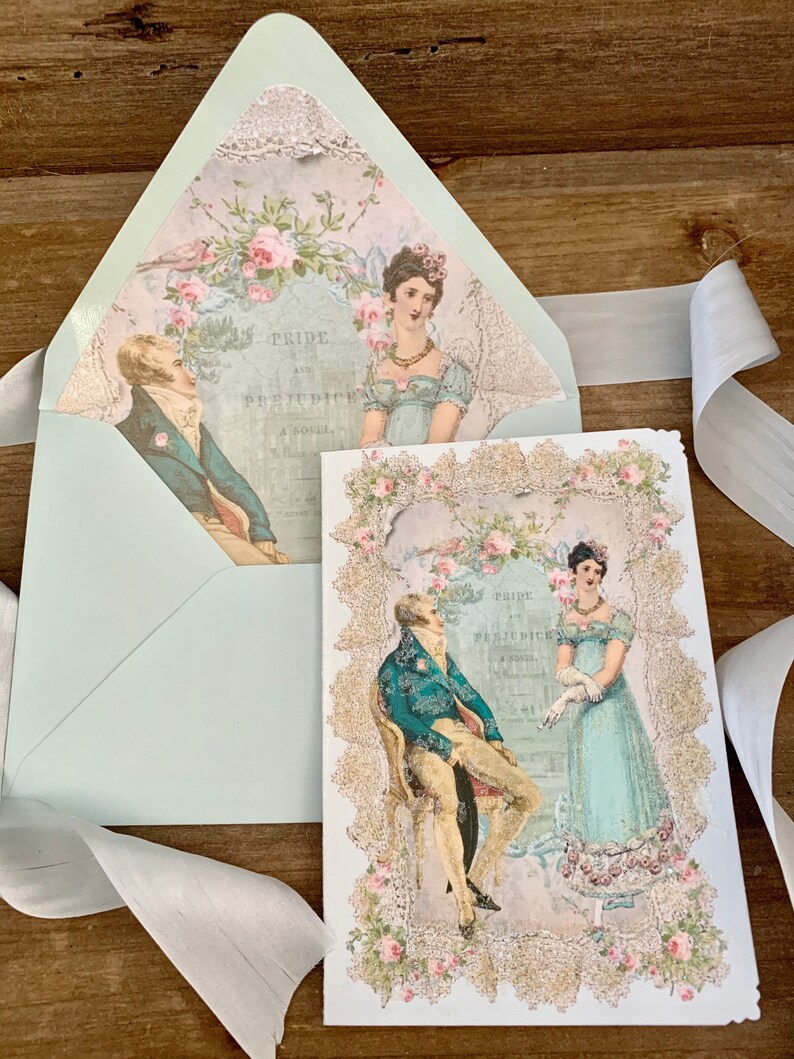 May include: A light blue envelope and card set featuring illustrations from "Pride and Prejudice." The card and envelope interior display images of a man and woman in period attire, surrounded by floral and lace embellishments. The text "Pride and Prejudice" is visible.