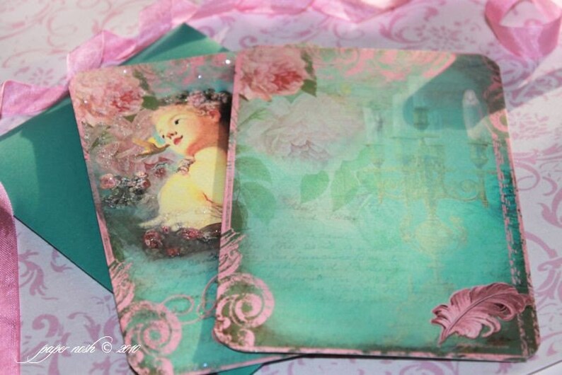 May include: Two teal green cards with pink floral designs and a pink feather on one card. The cards have a vintage aesthetic and are perfect for scrapbooking or crafting.