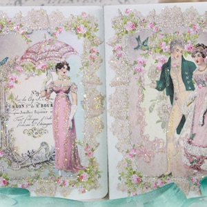 May include: A decorative journal featuring vintage illustrations of people in period clothing. The pages are framed with lace and floral accents, with glitter embellishments. The journal has a romantic, antique aesthetic.