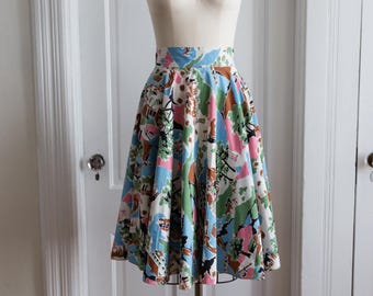 May include: A full-circle skirt with a white background and a colorful abstract print. The skirt has a high waist and a fitted bodice. The print features shades of blue, pink, green, and brown.