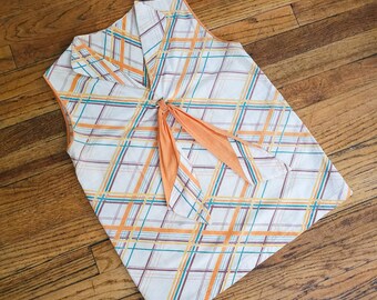 May include: A sleeveless blouse with a plaid pattern in shades of orange, brown, and blue on a white background. The blouse has a tie at the neck.