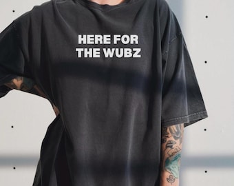 May include: Dark gray t-shirt with the text "HERE FOR THE WUBZ" in white block letters. The shirt has a slightly faded appearance and a relaxed fit. The model is wearing the shirt.