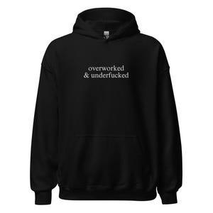 May include: Black hoodie with the white text "overworked & underfucked" across the chest. The sweatshirt features a hood with a drawstring and a front pocket. The material appears soft and comfortable.